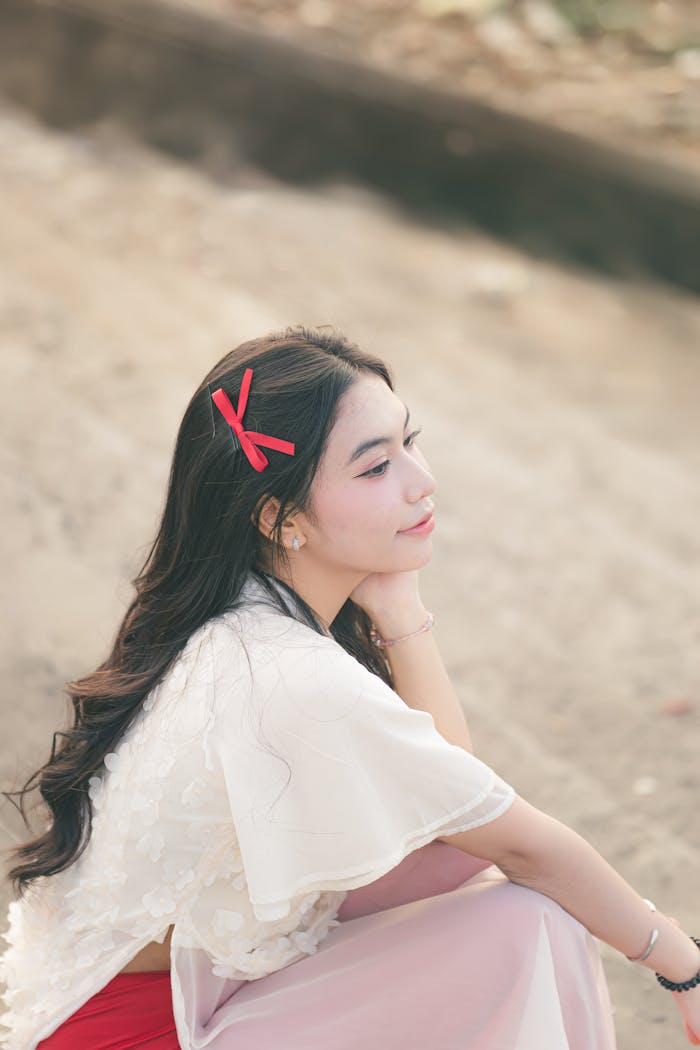 Elegant woman with a red bow in hair sitting outdoors. Soft, dreamy mood.